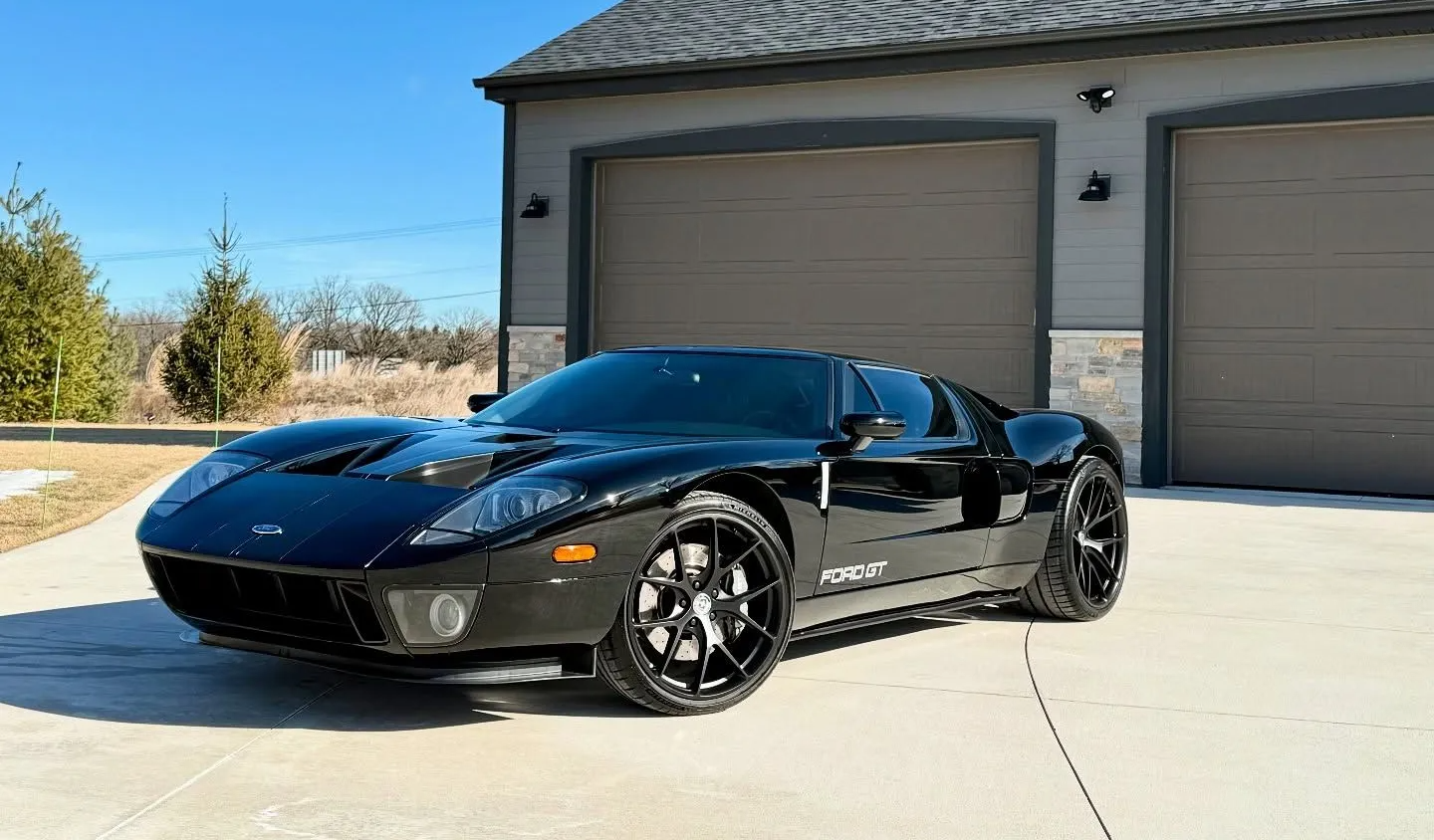 Black sports car parked in front of a garage on a sunny driveway