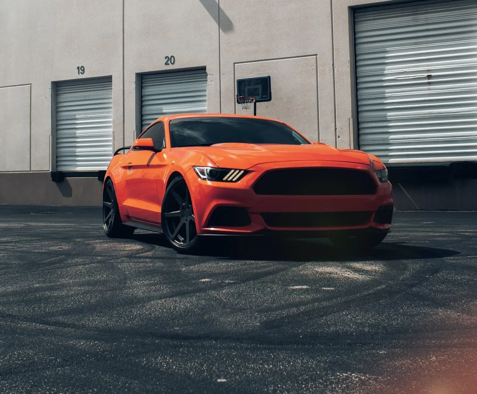 Orange sports car parked outside industrial building with roll-up doors