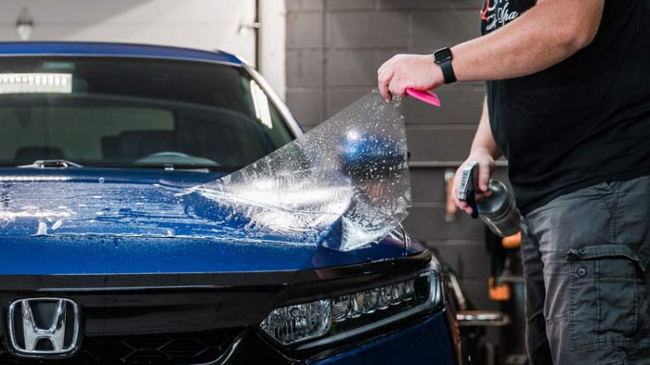 Person pressure-washing the front of a blue Honda car in a garage