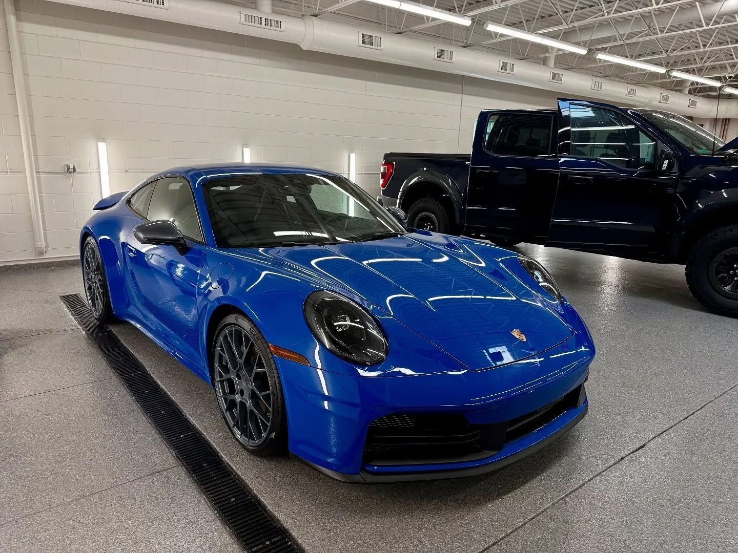 Blue sports car parked indoors beside a black pickup truck.