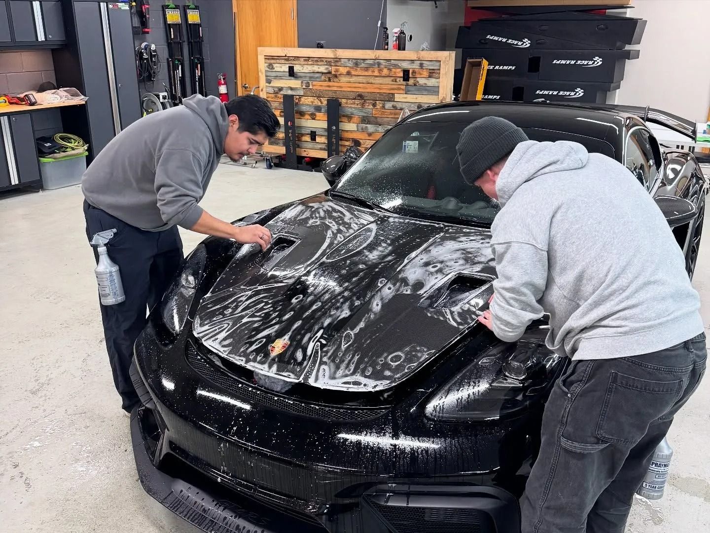 Two people washing a black sports car inside a garage.