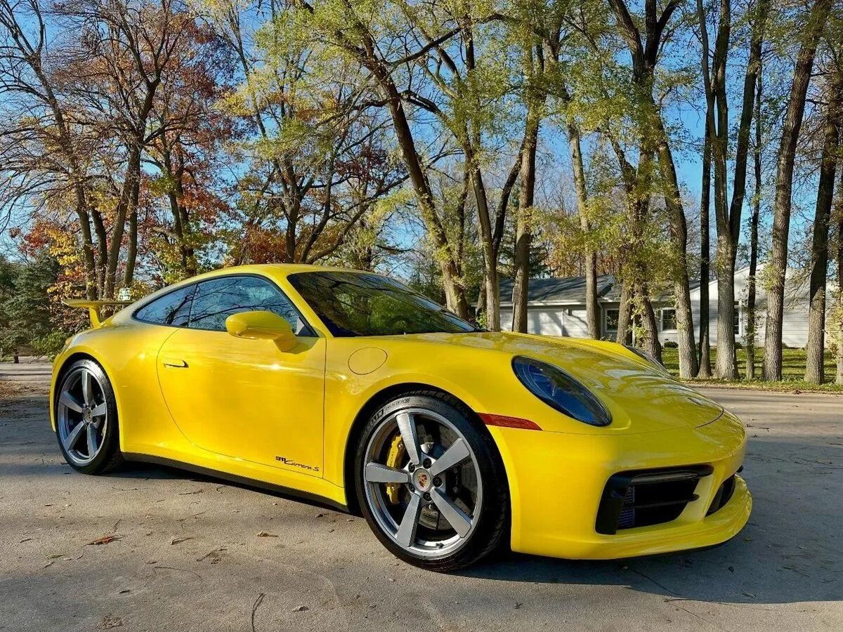 Yellow sports car parked on a tree-lined road in autumn sunlight
