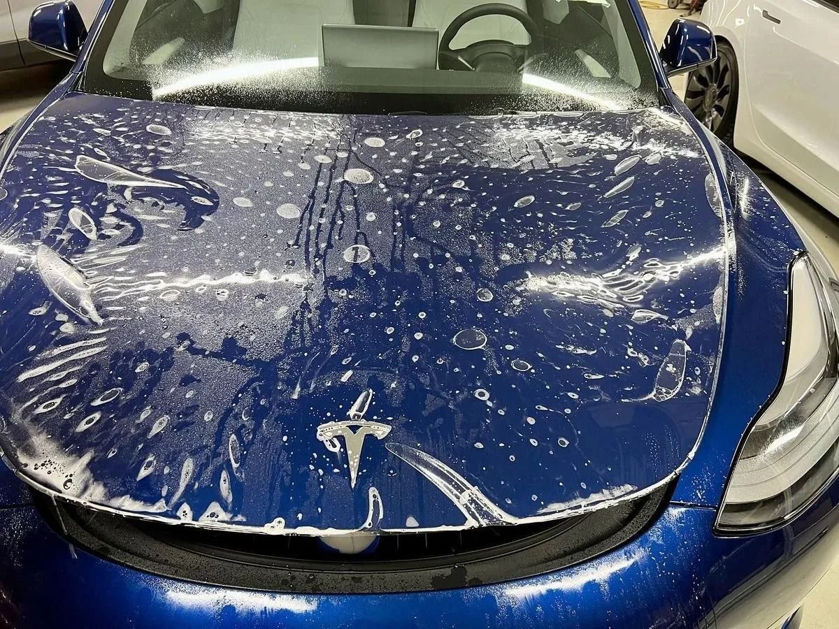 Blue Tesla sedan covered in soap suds, front view in a car wash