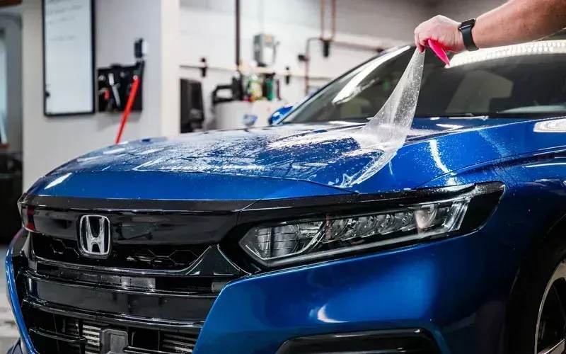 Blue Honda sedan being washed with a hose at a car wash