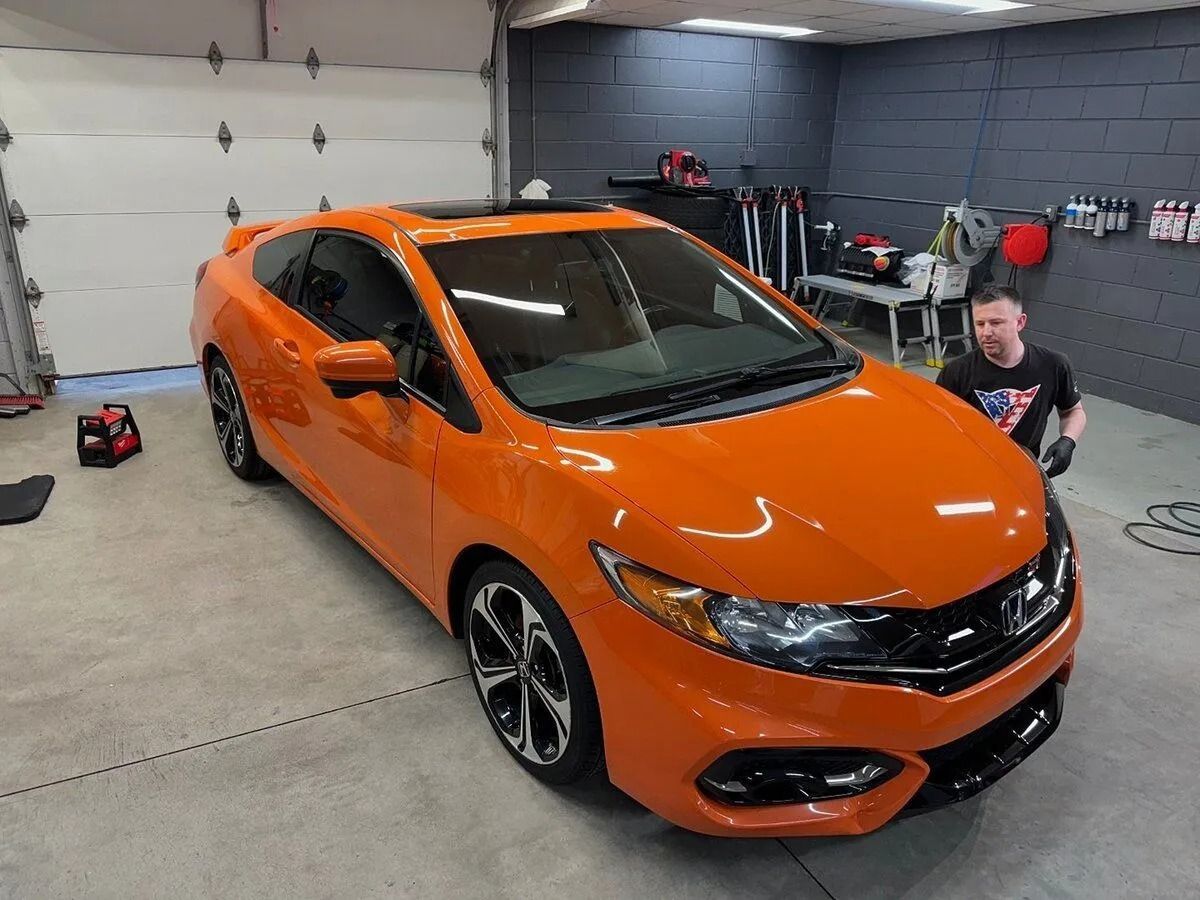 Orange sedan in a garage, with a person crouching beside it.