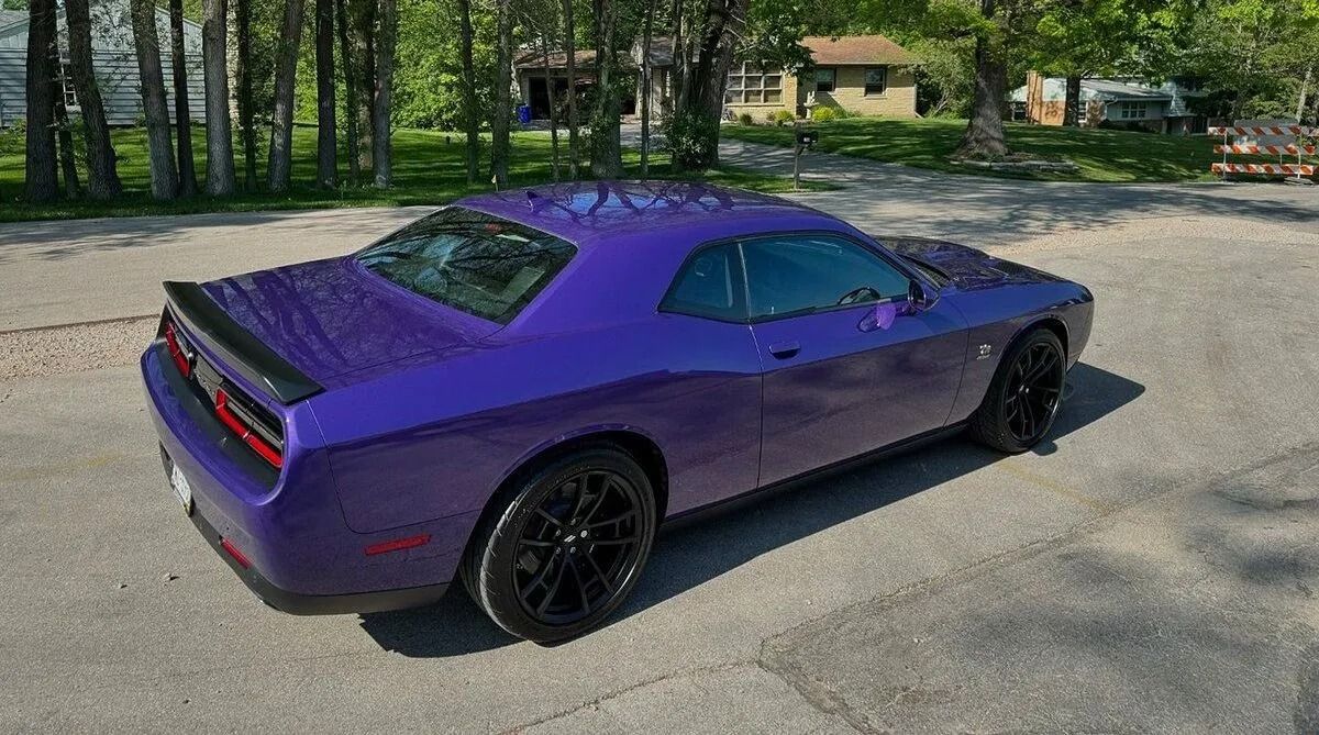 Purple sports car parked on a driveway with trees and houses in the background