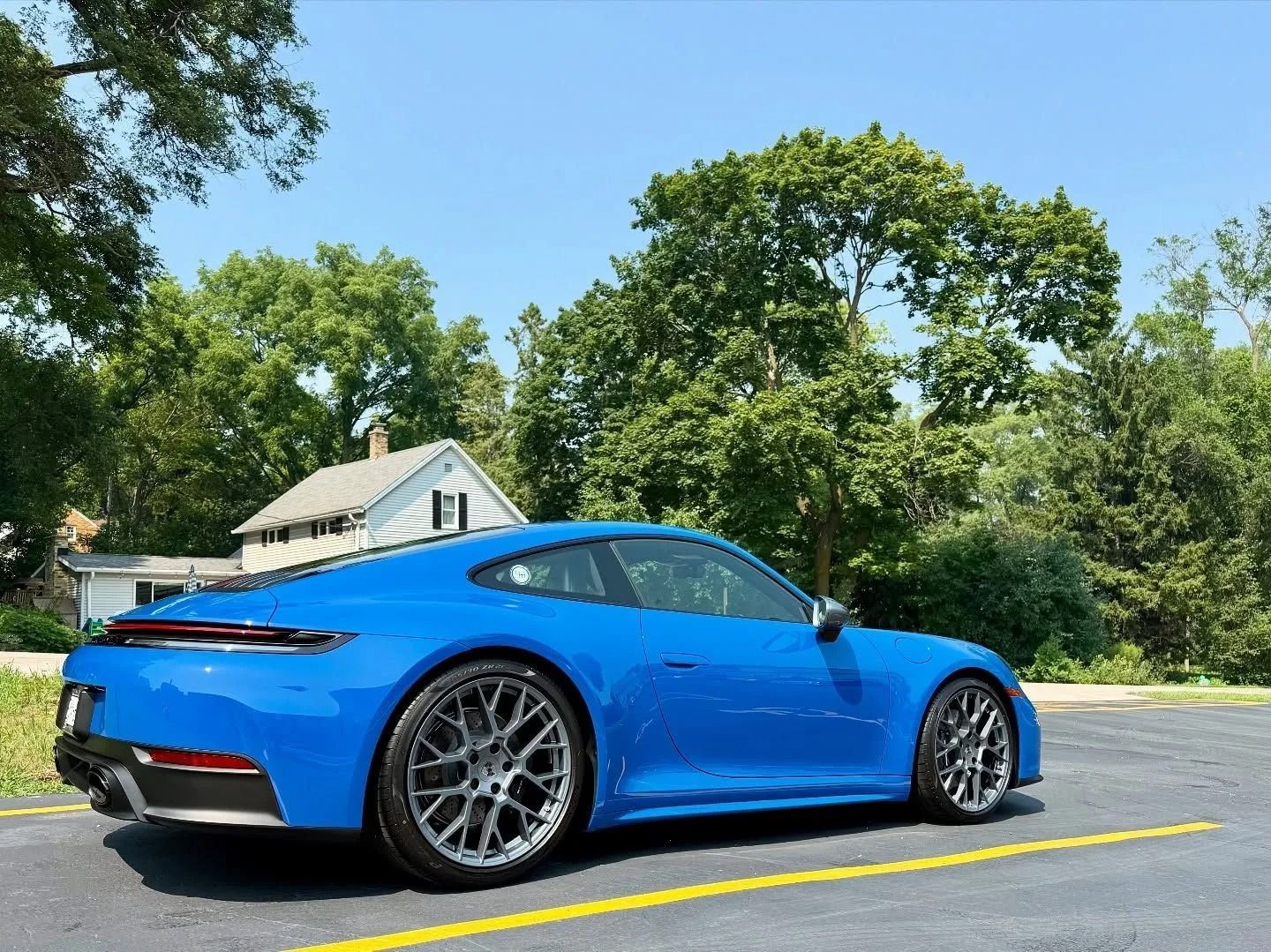 Blue sports car parked on a road beside trees and a house on a sunny day