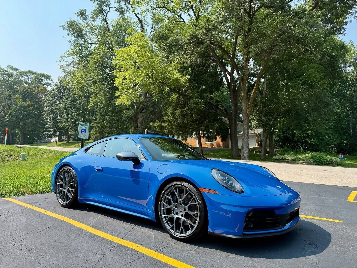 Blue sports car parked on a road beside grass and trees on a sunny day