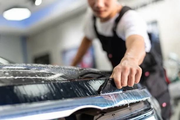 Worker squeegeeing water off a car windshield in an auto shop