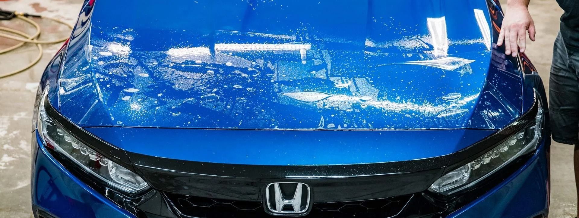 Blue Honda sedan with shattered windshield and water spray, front view