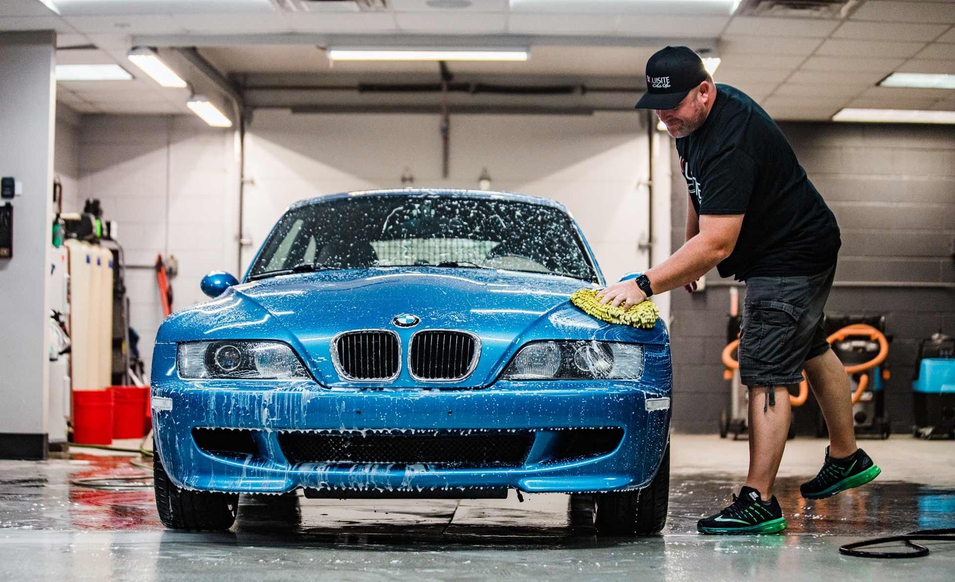 Blue sports car being washed by a person in a garage-like car wash bay