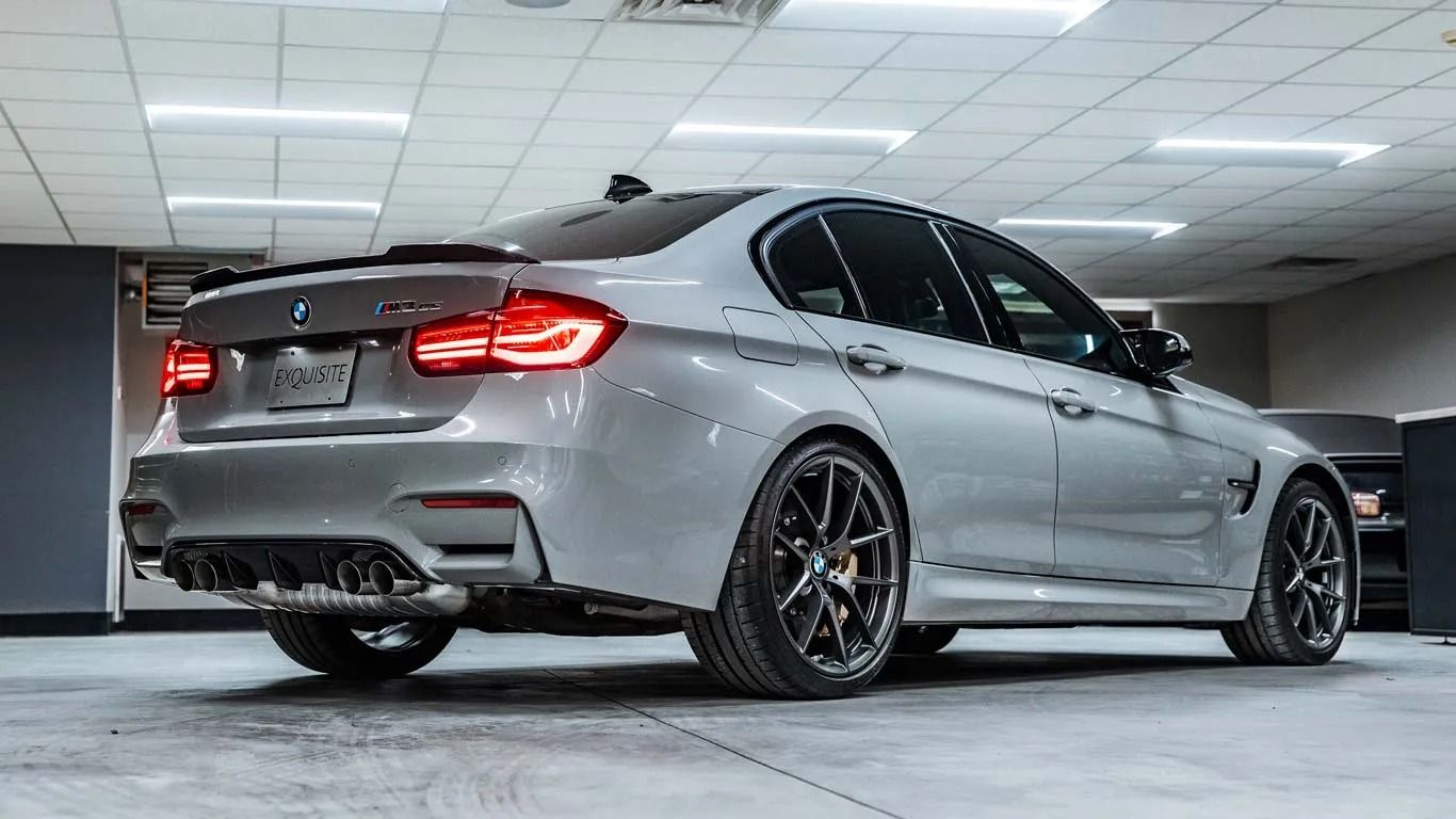 Silver sports sedan with black wheels parked in a garage, rear three-quarter view
