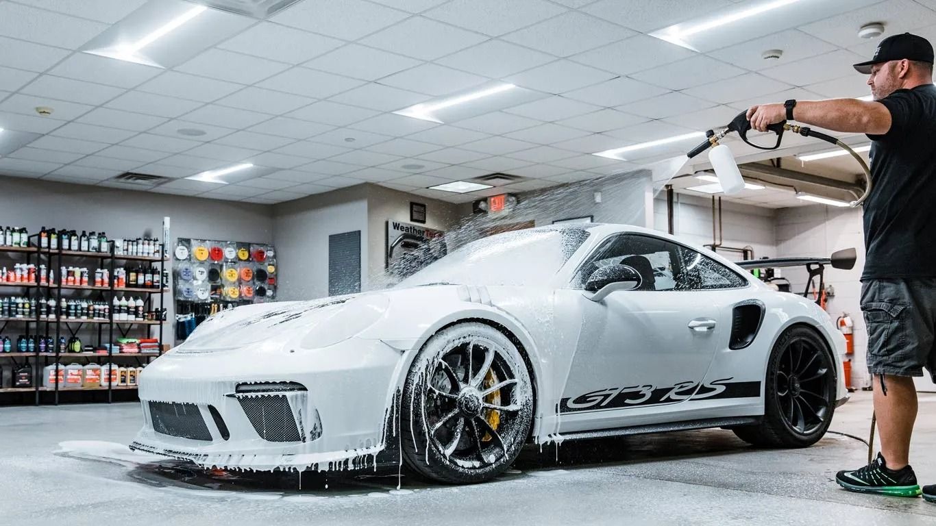 White sports car being sprayed with foam in a car wash bay, with a worker rinsing it off.