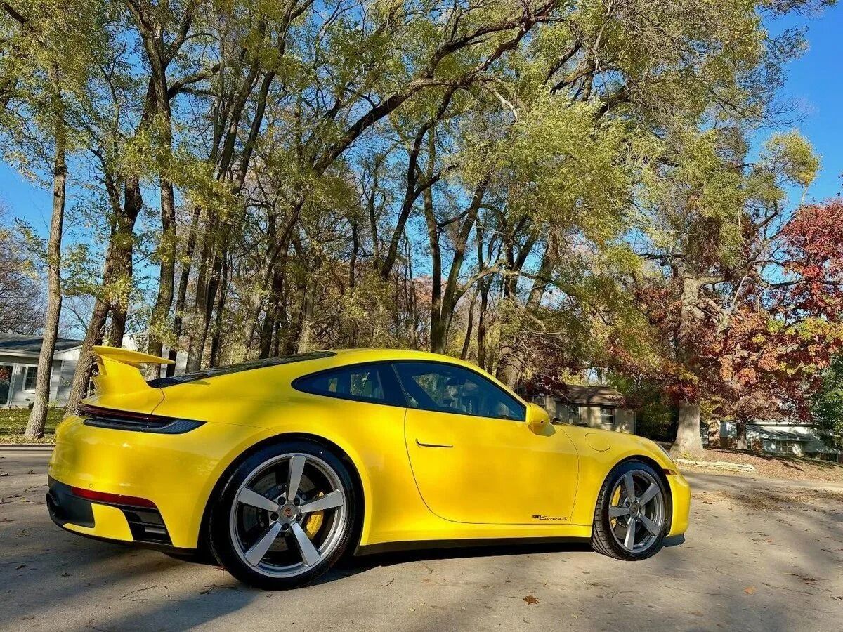 Yellow sports car parked on a sunny street with trees in the background