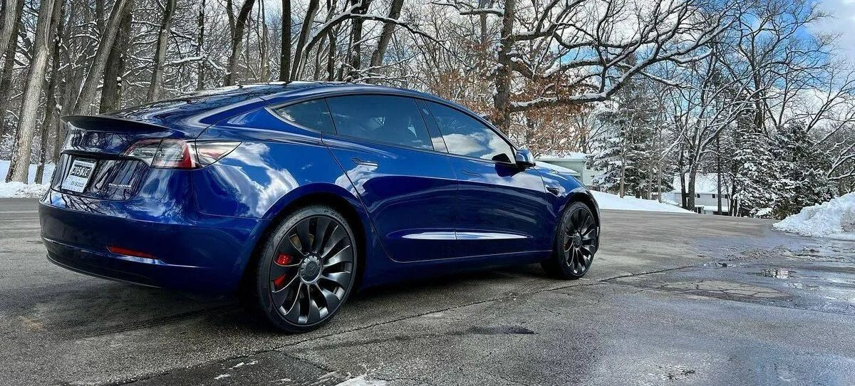 Blue sedan parked on a snowy road with bare trees in the background.