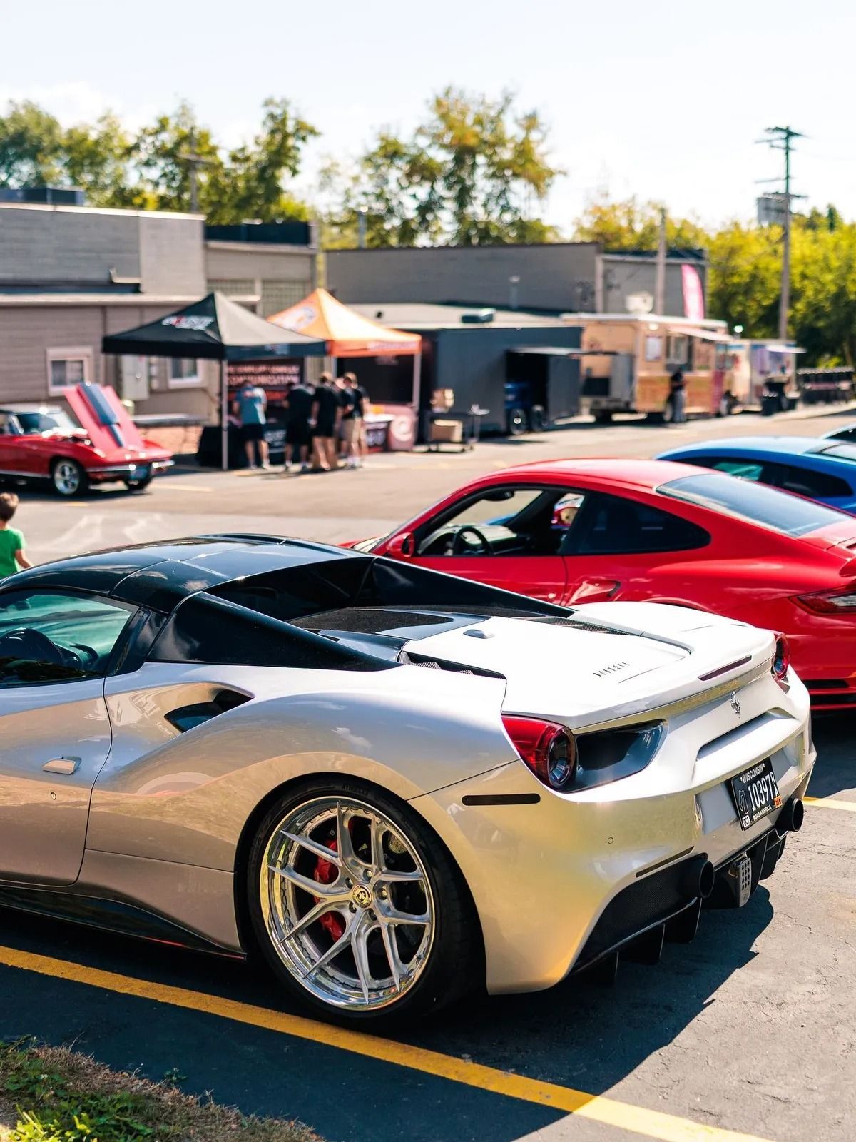 Silver sports car with red seats parked at a car show, with tents and other cars in the background