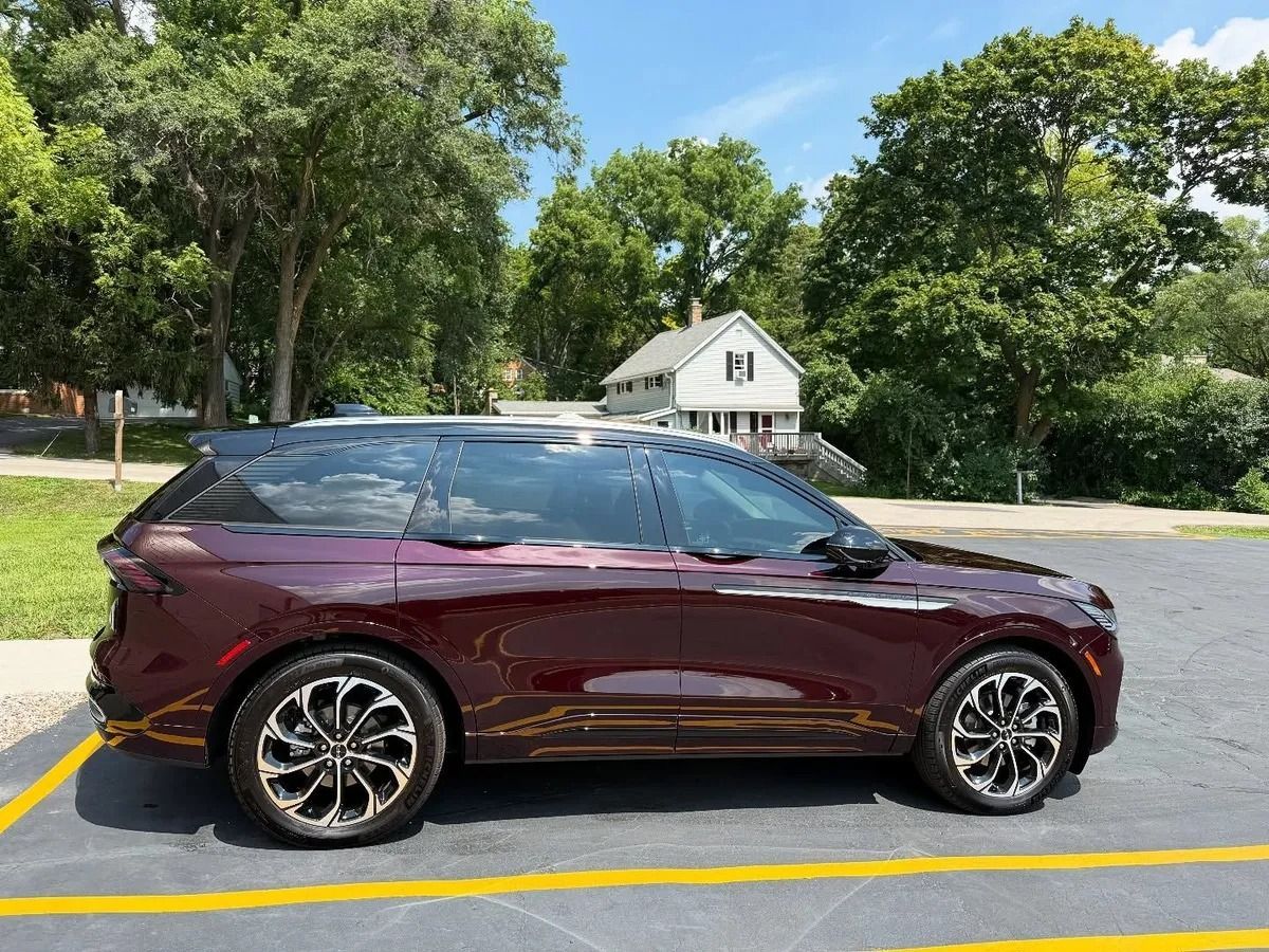 Maroon SUV parked in a lot with trees and a small house in the background