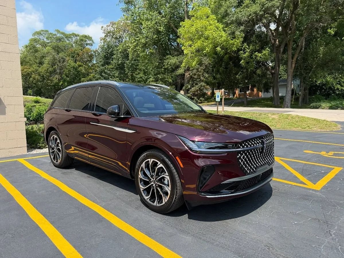 Maroon SUV parked in a marked lot beside a building, with trees and yellow curb lines nearby