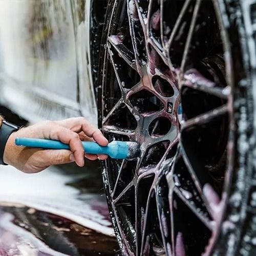 Hand washing a black alloy wheel with a blue brush and soapy water