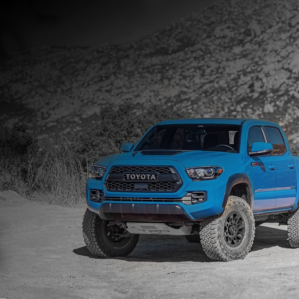 Bright blue Toyota pickup driving on a dusty road with rocky hills in the background