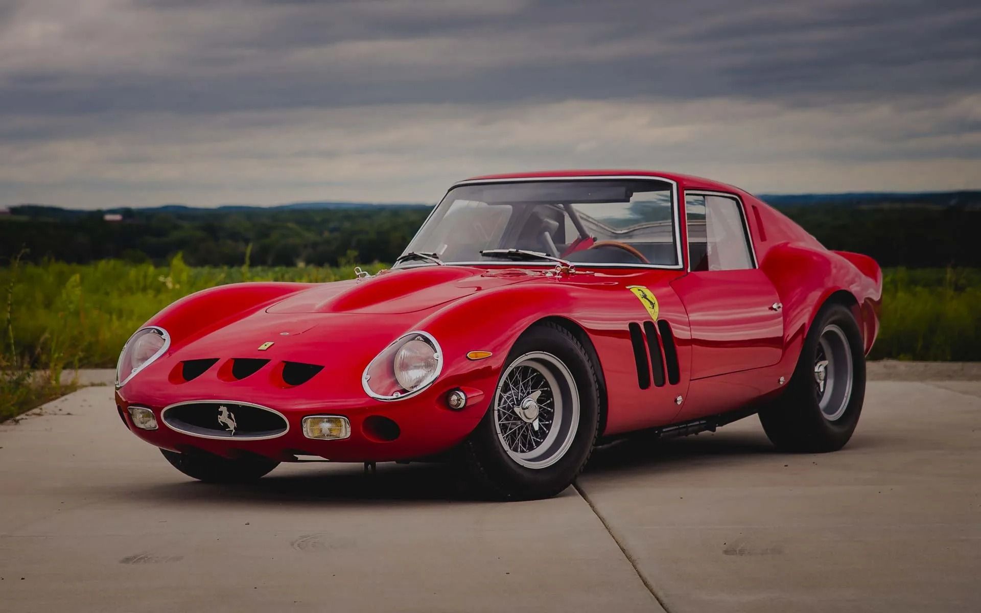 Red vintage sports car parked on a road with a cloudy landscape background.