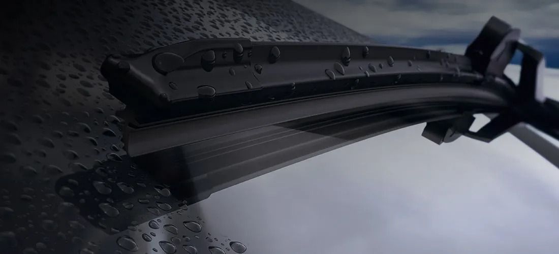 Close-up of a black windshield wiper on a rain-covered car windshield