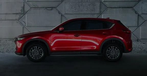 Red SUV in side profile parked indoors against a gray concrete wall.