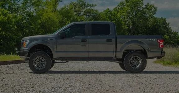 Gray pickup truck parked on a gravel road with trees in the background