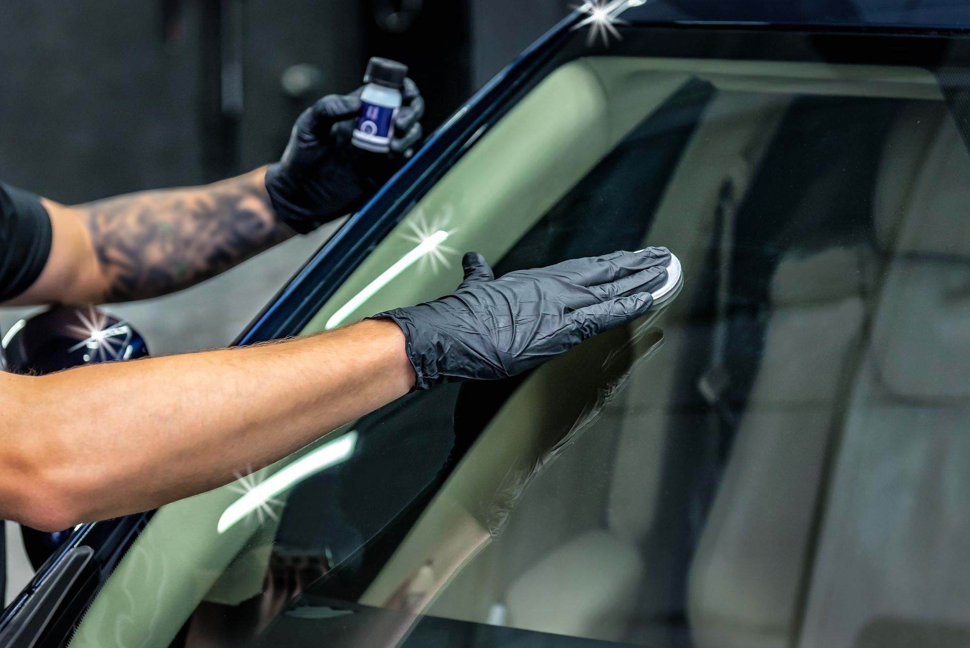 Gloved hands cleaning a car windshield with a spray bottle and cloth