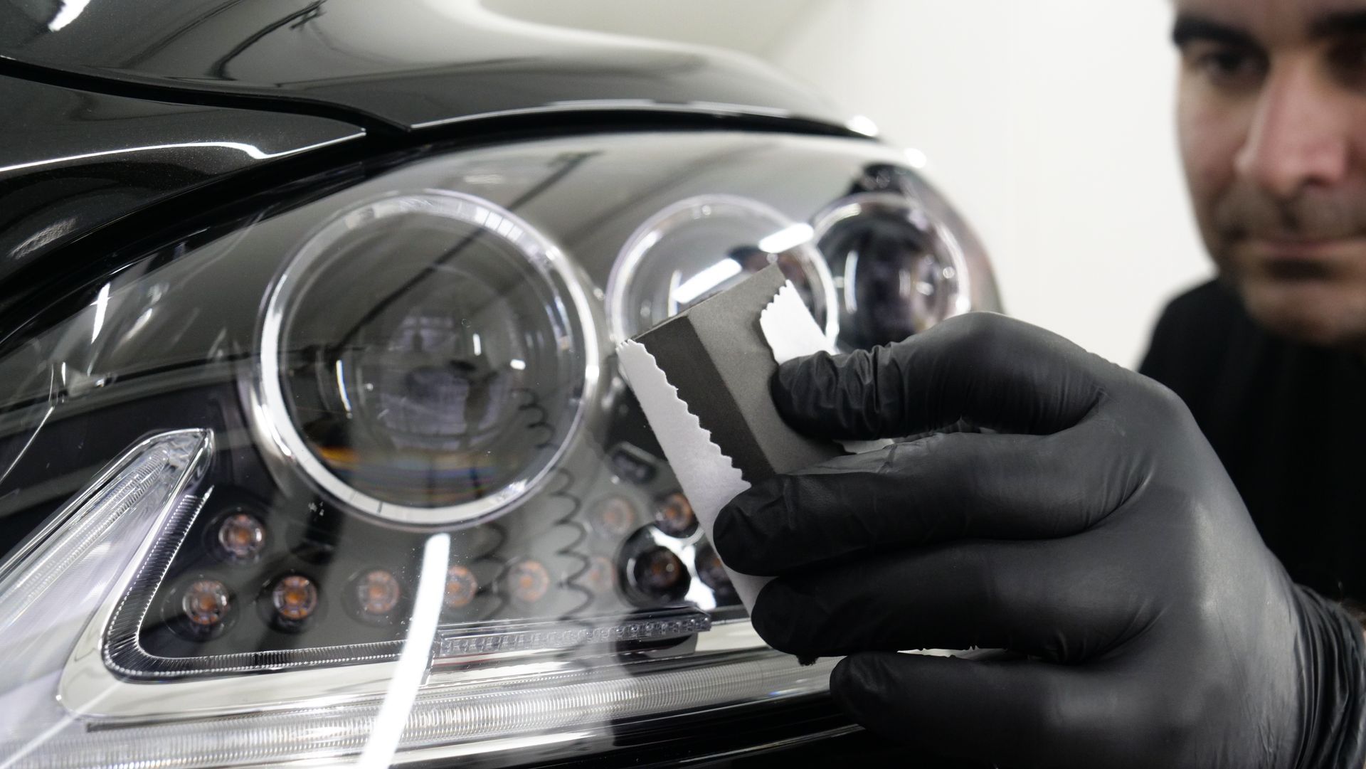 Gloved hand polishing a car headlight with a cloth, showing reflective chrome details.