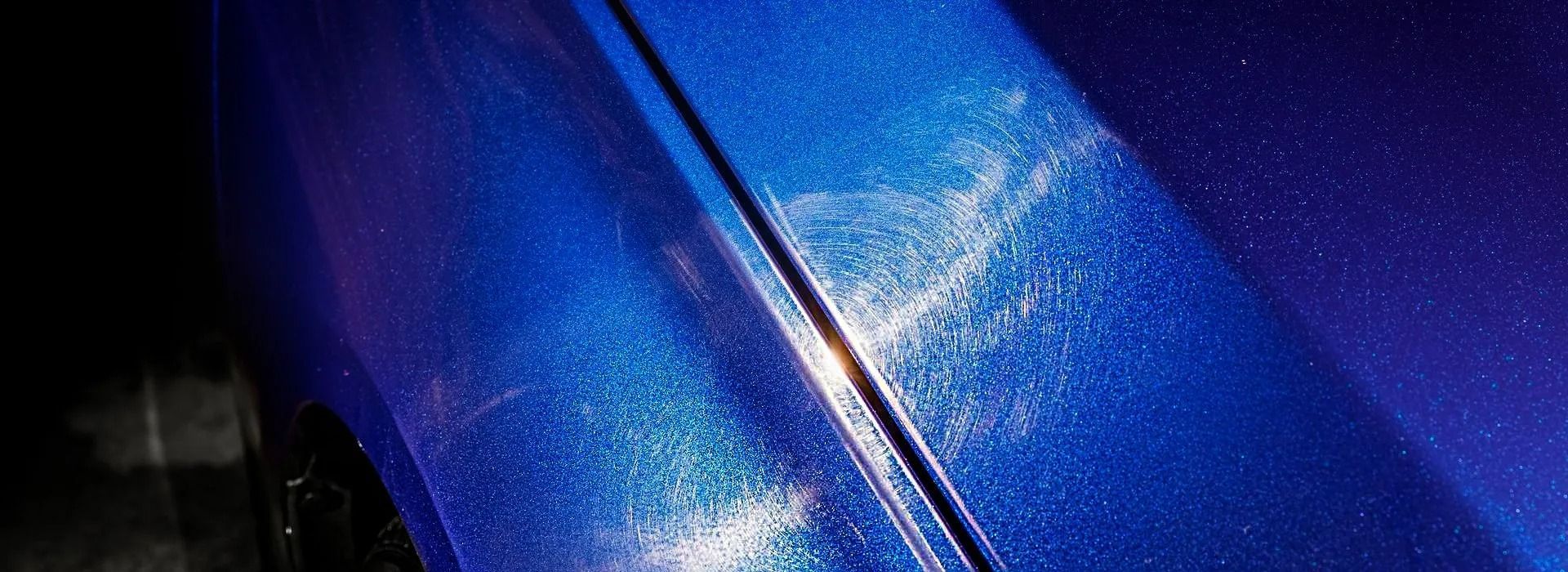 Close-up of a blue car hood with metallic paint and water droplets, reflecting sunlight
