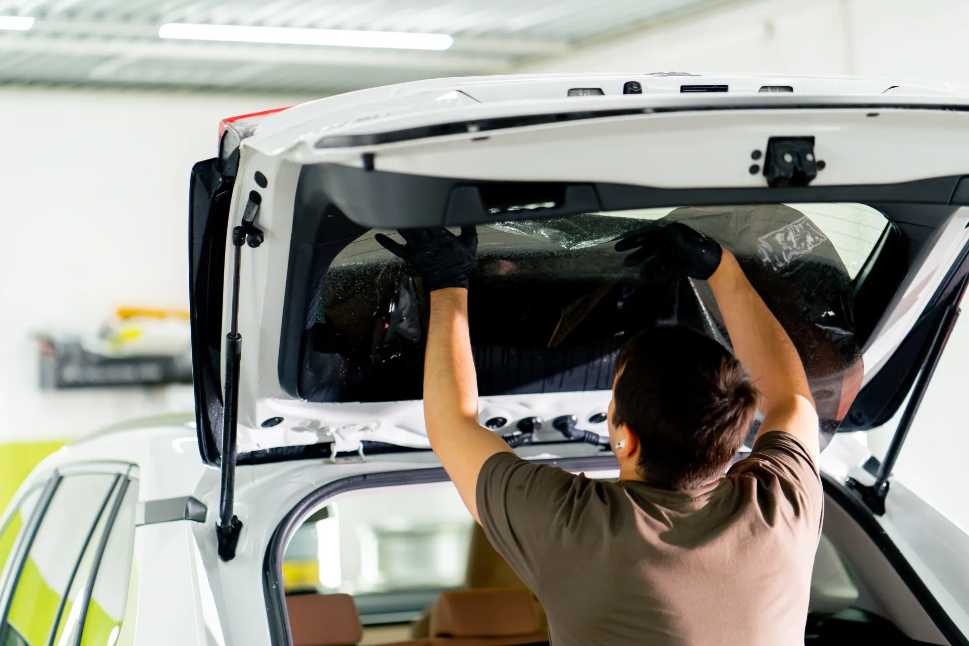 Person installing a rear window on a white car in a garage