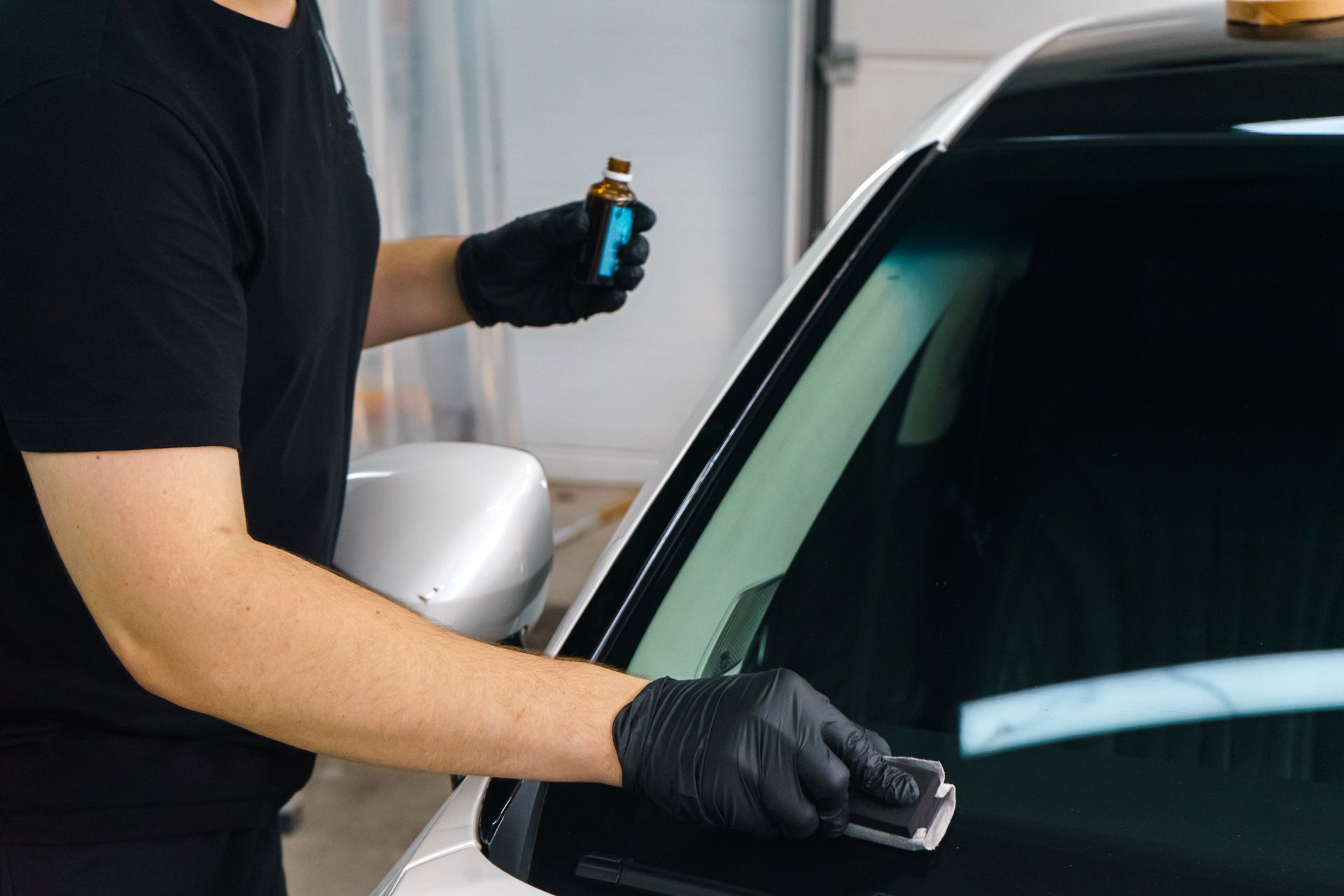 Person in black gloves cleaning a car windshield with spray bottle and cloth
