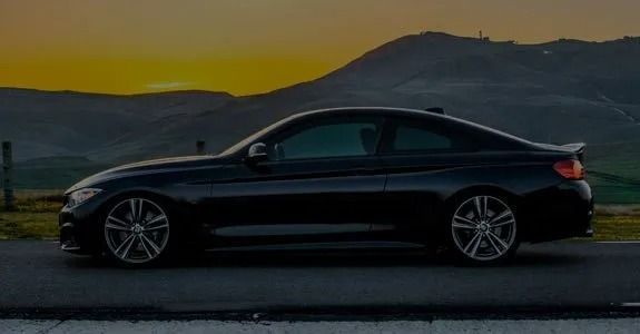 Black sports coupe parked on a road at dusk with mountains in the background