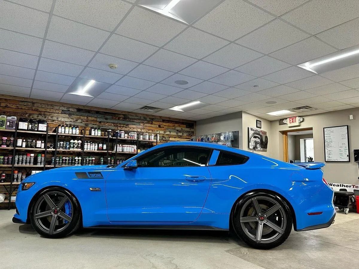 Blue sports car parked indoors in a garage showroom under fluorescent lights