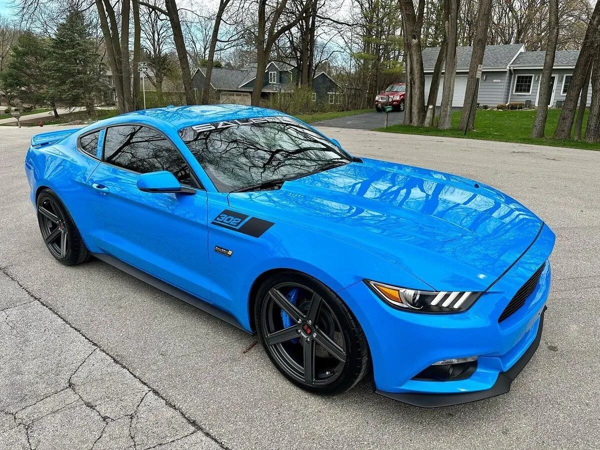 Blue sports car parked on a driveway with trees and a house in the background