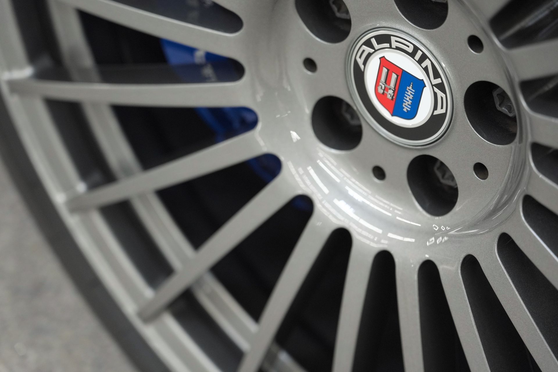 Close-up of a silver Alpina car wheel rim with blue and red center badge
