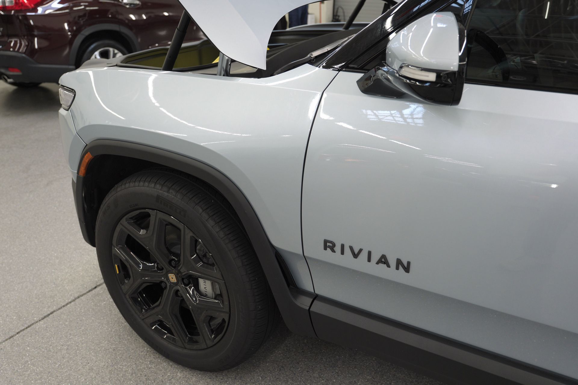 Close-up of a white Rivian SUV’s front side with black wheel in a showroom