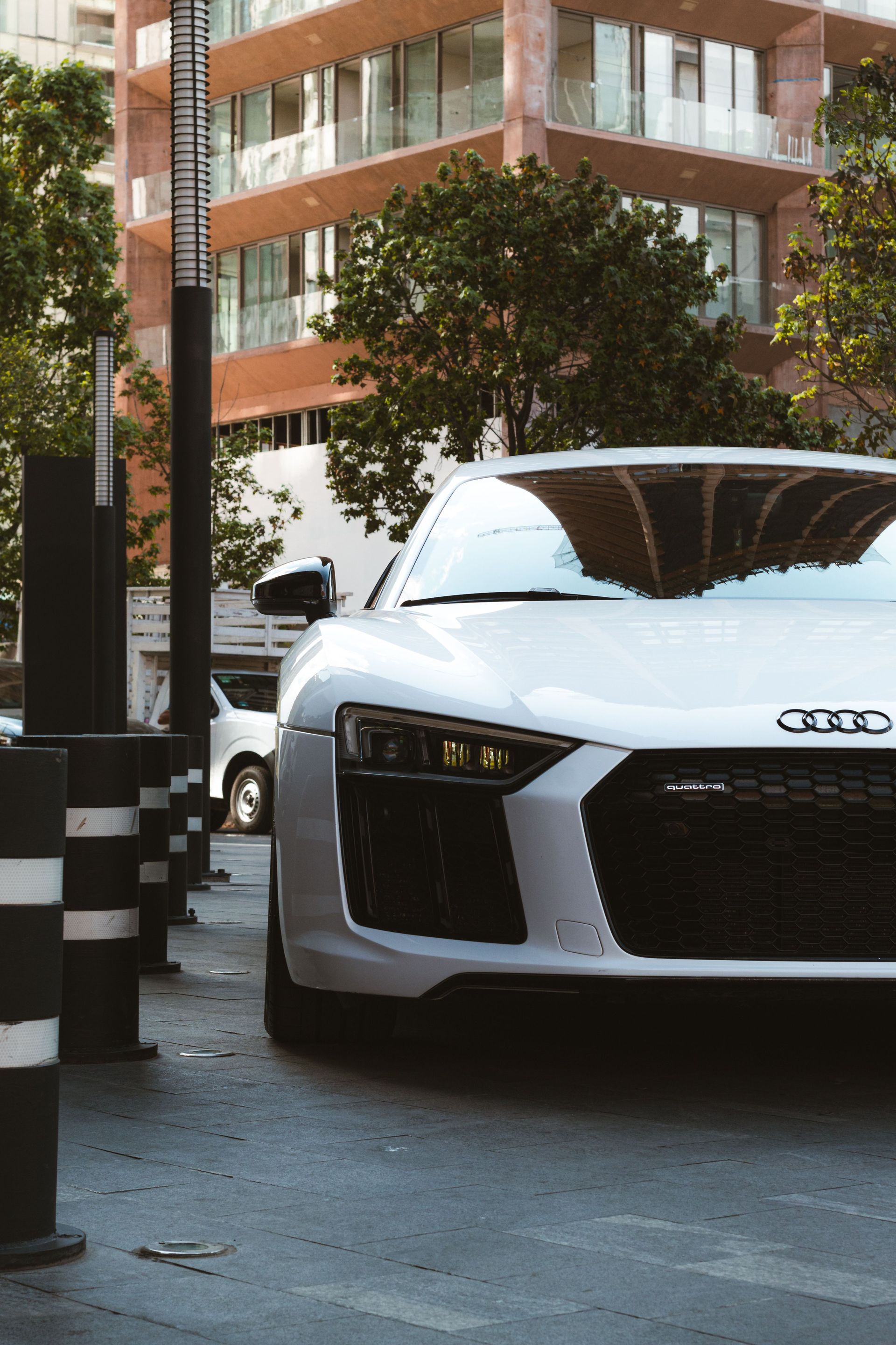 White Audi parked on a city street beside black-and-white bollards and a modern building
