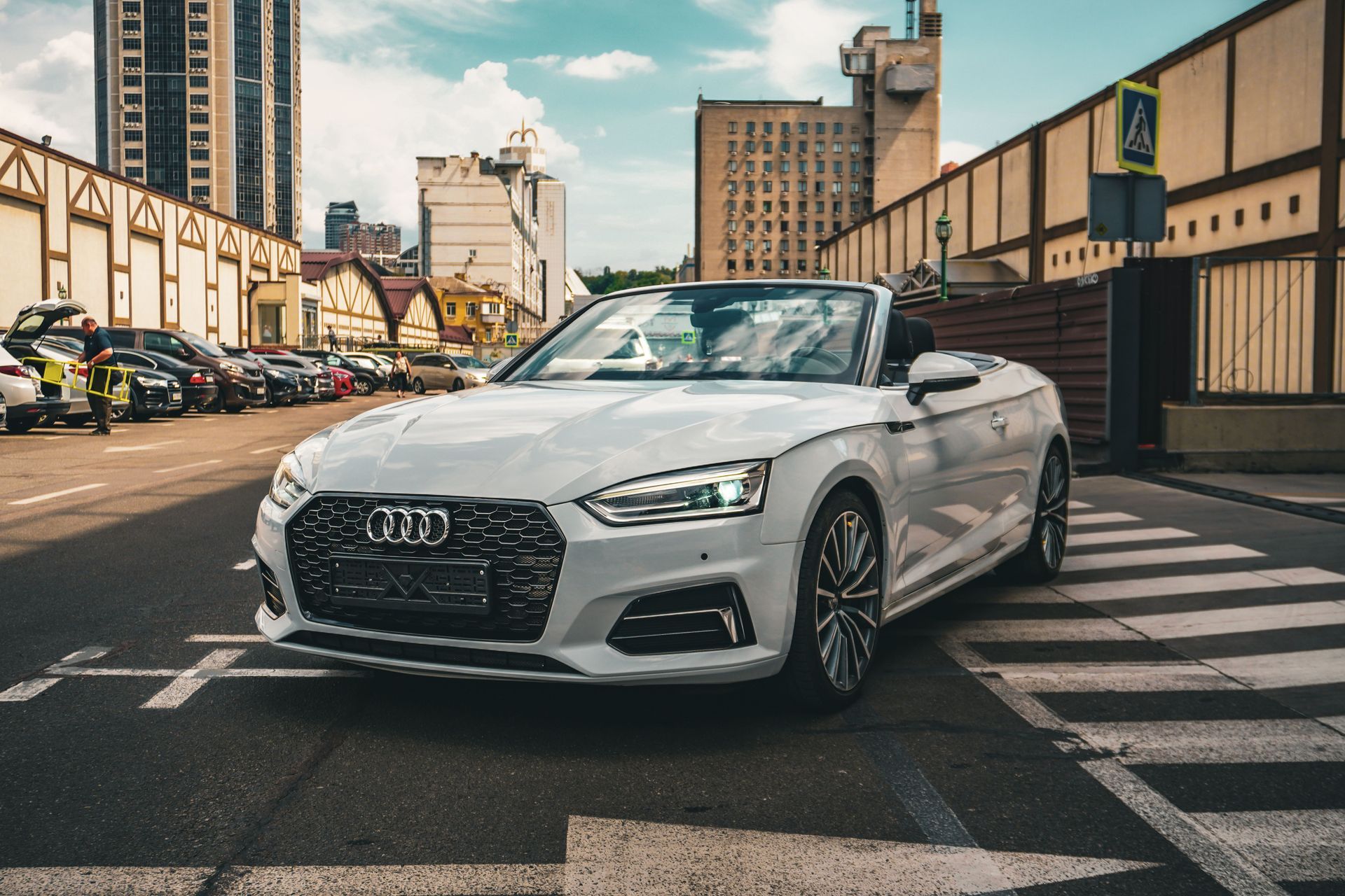 White Audi convertible parked on a city street with buildings and crosswalks in the background