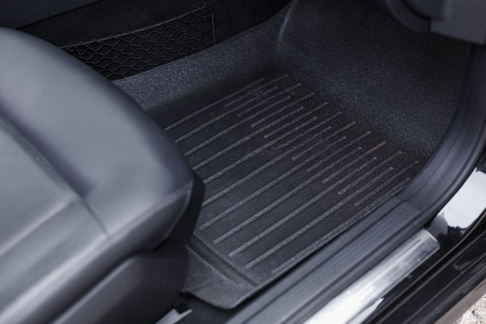 Car interior with rear seat and tan woven floor mat covering the footwell