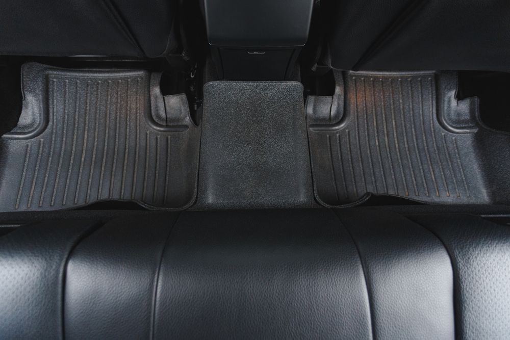 Car floor mat with raised edges and textured grooves in a car’s front footwell