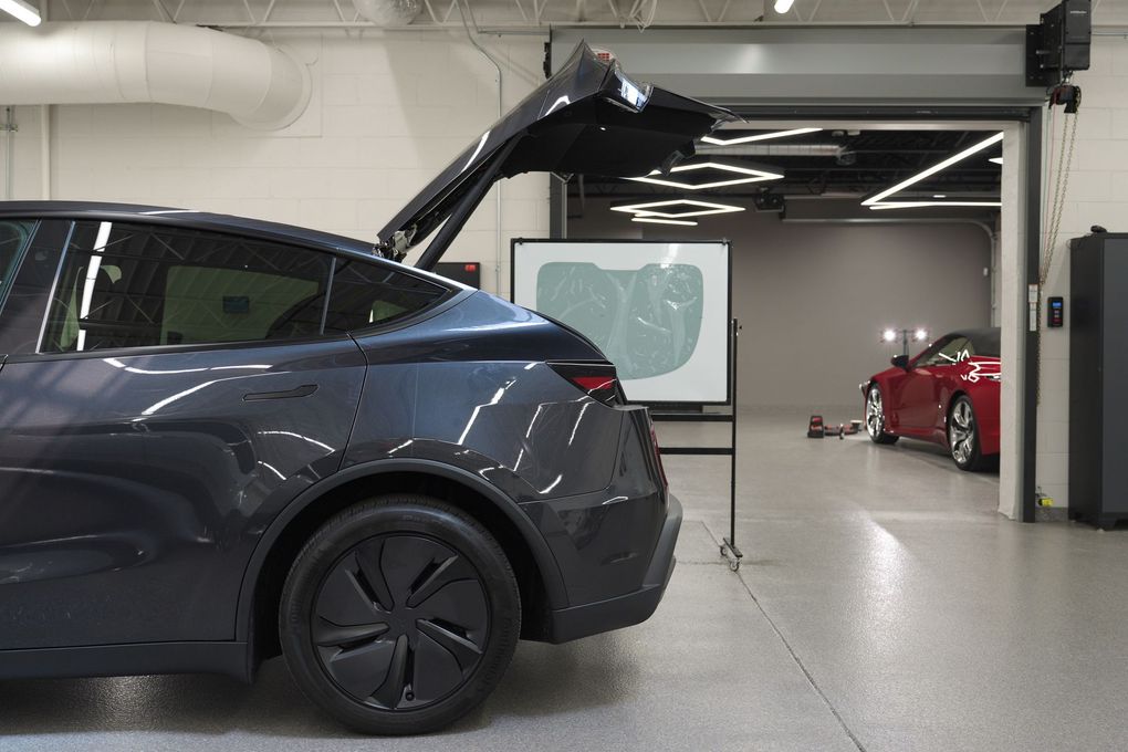 Dark blue SUV with open rear hatch in a garage, with a red car in the background.