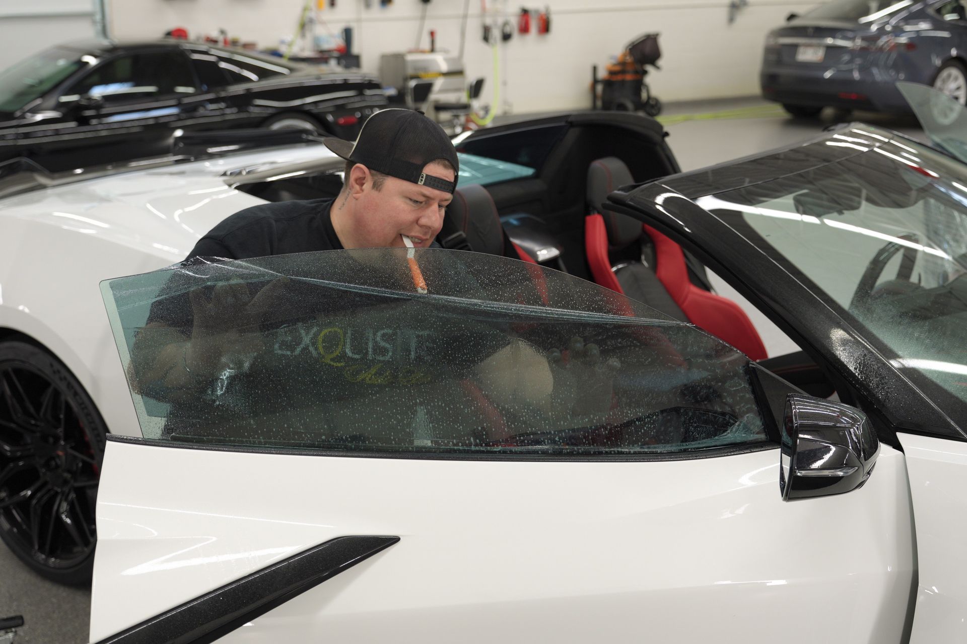 Man leaning into a white sports car with a cracked windshield in a garage