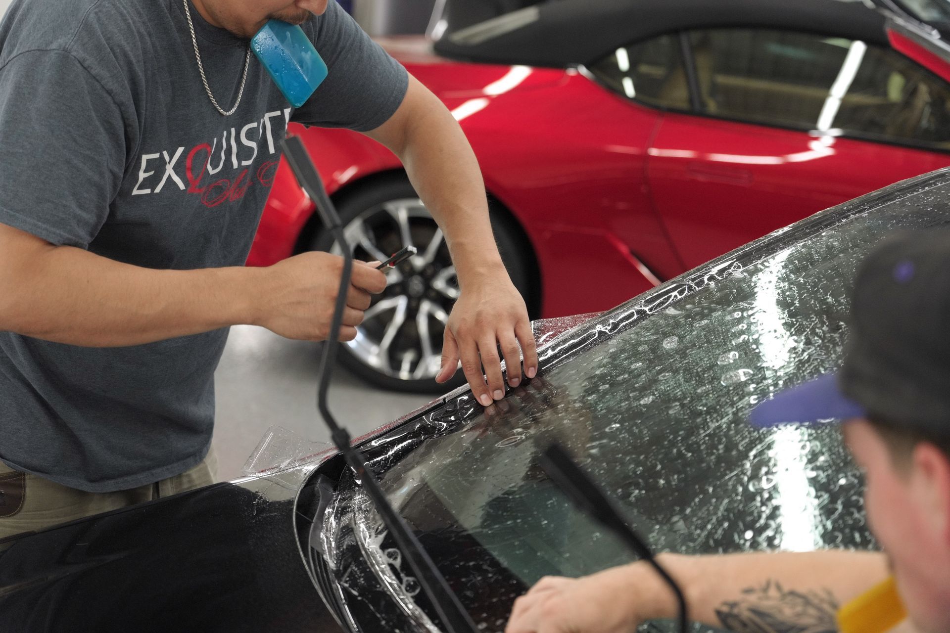 Person cleaning a black car windshield with a pressure washer in a car wash