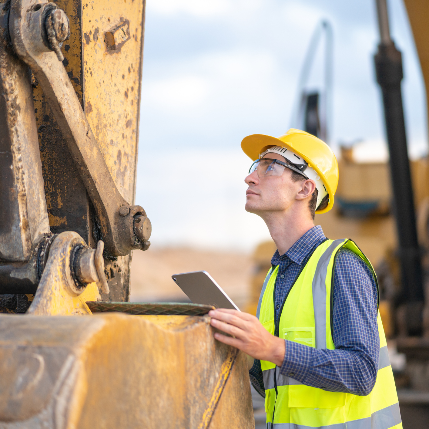 A Construction Worker Looks at A Tablet While Standing Beside a Bulldozer. A construction worker is looking at a tablet while standing next to a bulldozer.