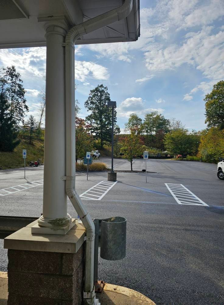 An asphalt parking lot with multiple blue-marked accessible parking spaces, viewed from under a building's porch pillar.