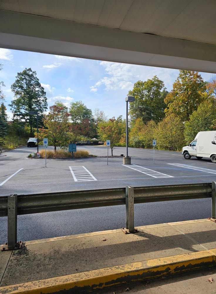An asphalt parking lot with multiple marked accessible parking spaces, signs, a small garden island, and trees.