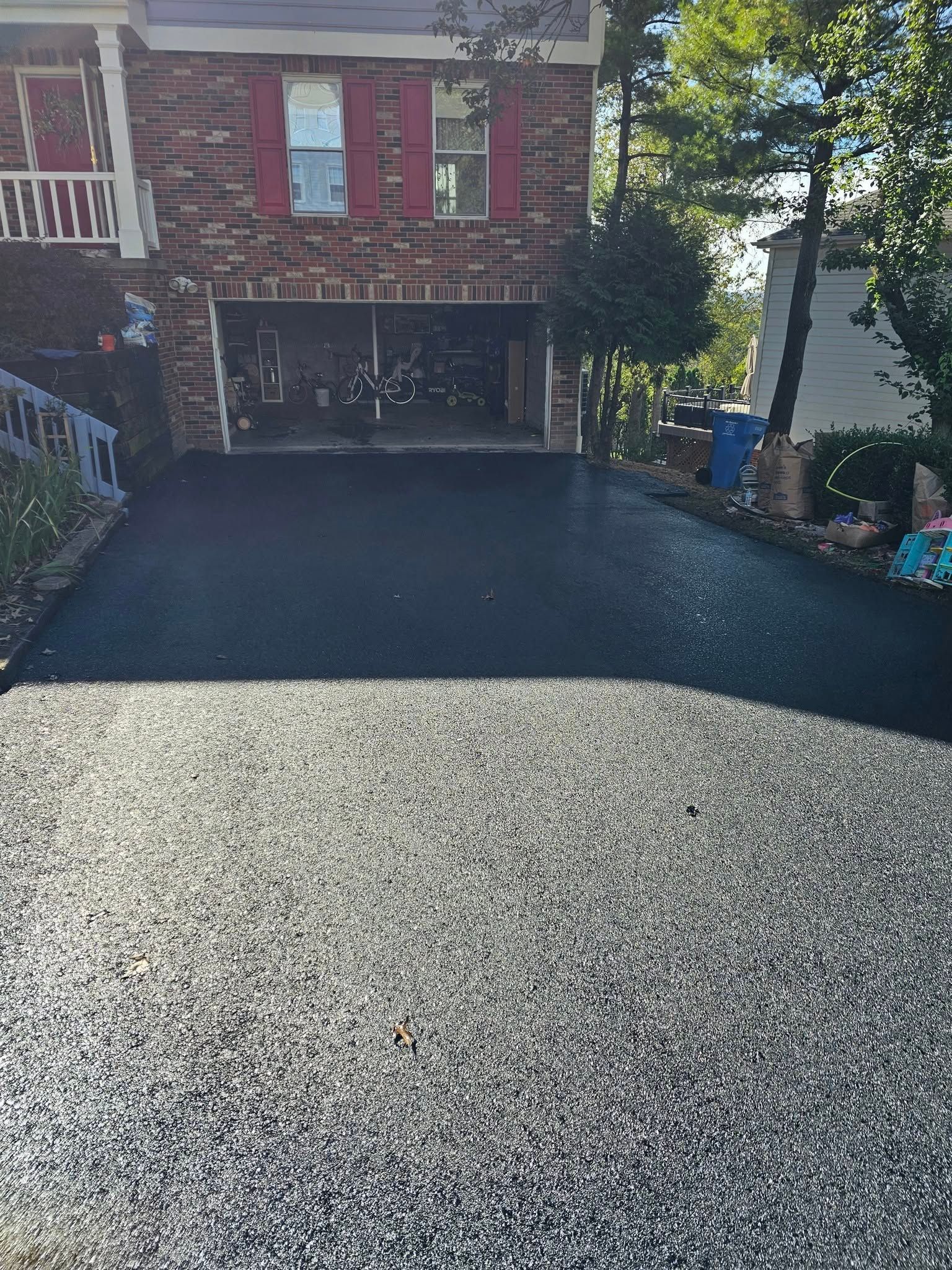 A two-tone driveway with textured gray aggregate in the foreground transitioning to smooth black asphalt near the house.