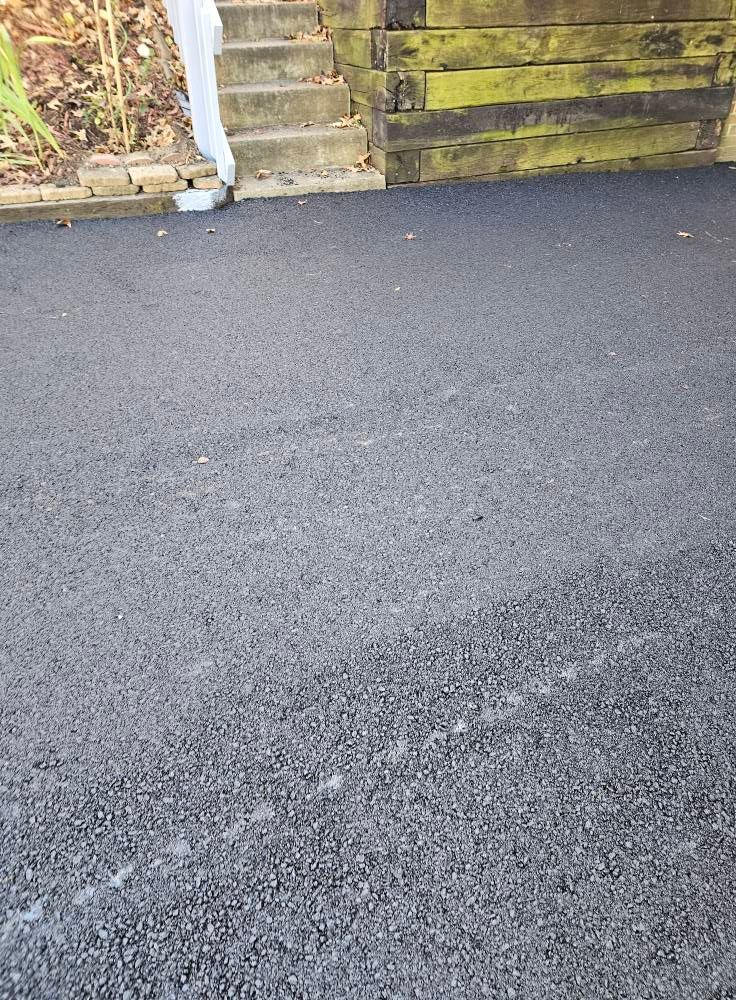 A freshly paved asphalt driveway surface leading to a set of stone steps and a wooden retaining wall.